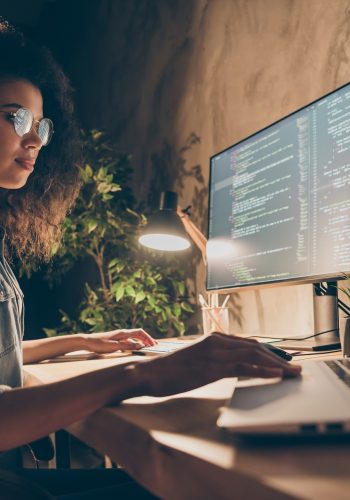 Profile side photo of concentrated skilled web expert afro american girl sit evening, desk use computer netbook work java script html back-end algorithm in workstation workplace